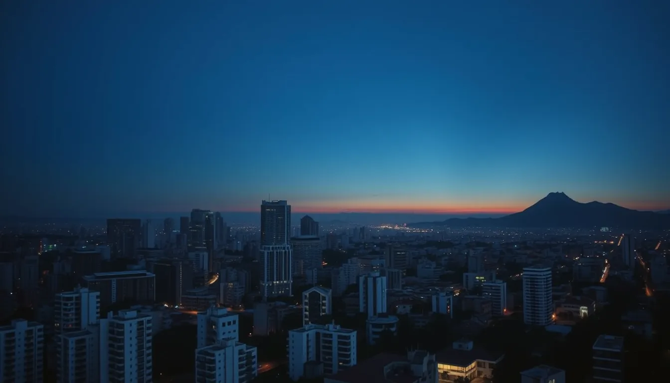 Vista aérea de uma cidade brasileira ao entardecer, com torres de vidro e concreto recortadas contra o céu azul-noite e a serra ao fundo.