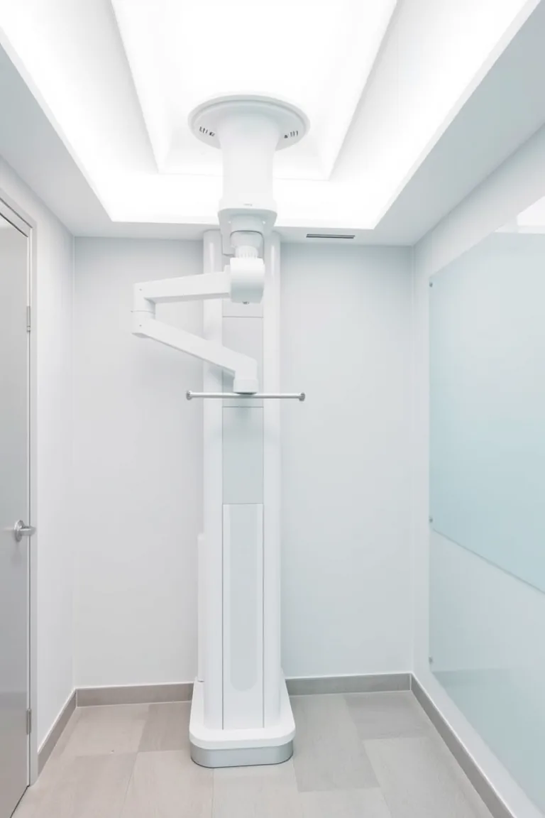 Aparelho de tomografia odontológica em sala clara, com arco articulado branco.